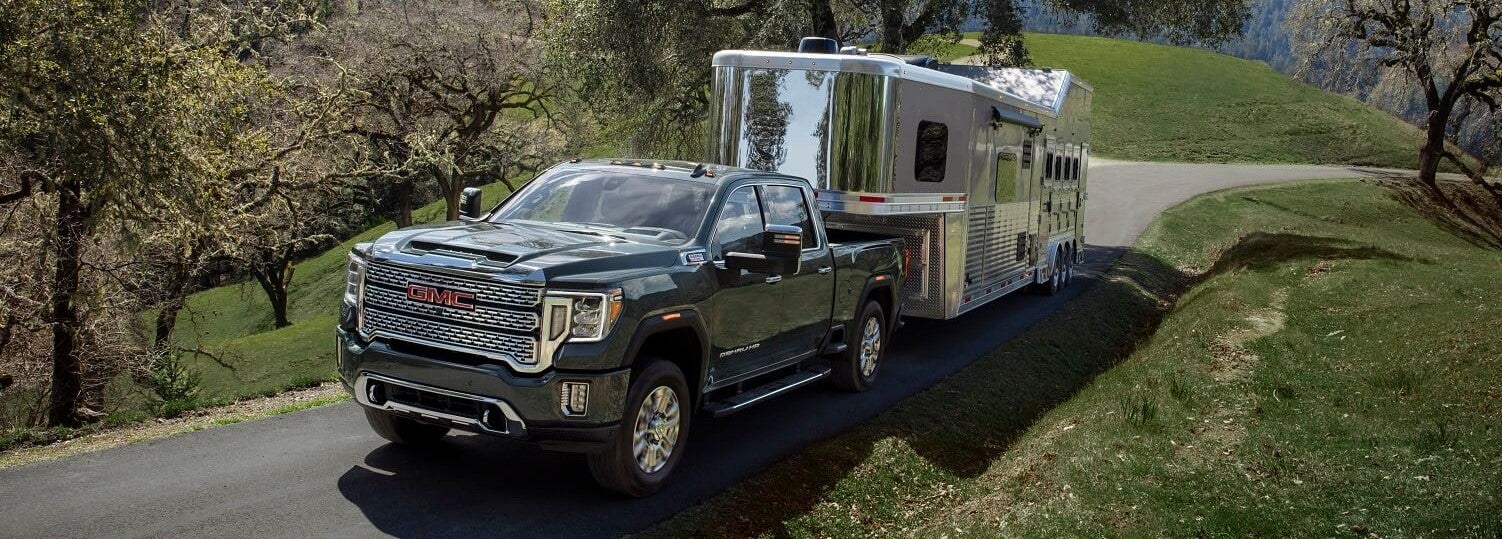 Black GMC Sierra 2500 towing a big trailer on a small pathway in a open, grassy area